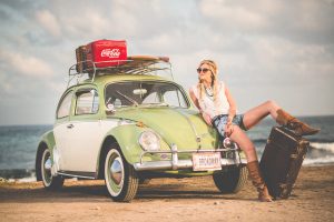 Jeune femme look vintage appuyée contre sapetite voiture verte avec valises sur le toit