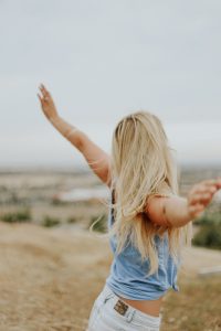 Jeune femme blonde de dos les bras écartés face au vent