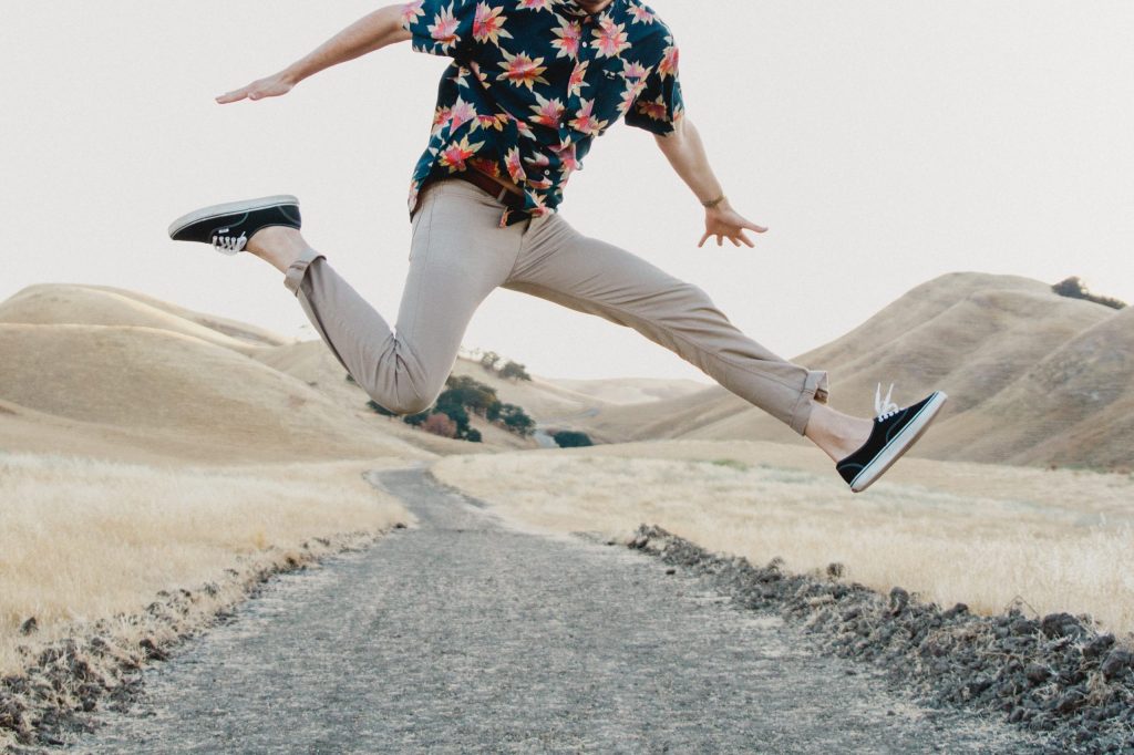 homme sautant dans les airs portant un chino clair et une chemise à motifs floraux