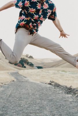homme faisant un saut dans les airs portant un chino clair et une chemise à motifs floraux